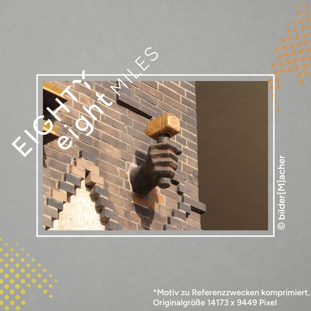 Wandbild einer Ziegelsteinmauer mit einer Skulptur, eine Hand mit einem Hammer in der Hand ragt zwischen den Ziegeln hervor