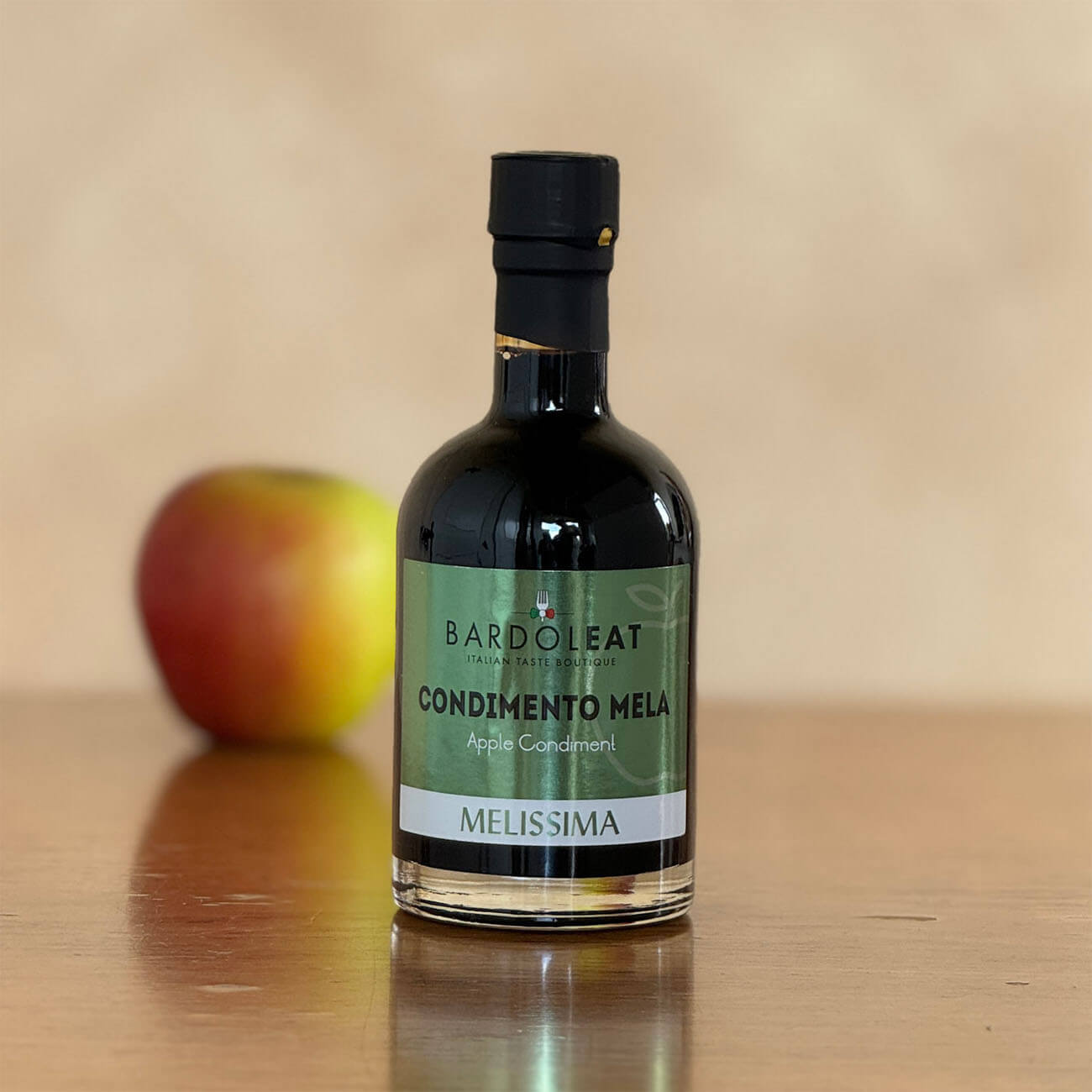 Eine Flasche des Essigs steht auf einem Holztisch. Im Hintergrund sieht man verschwommen einen Apfel.